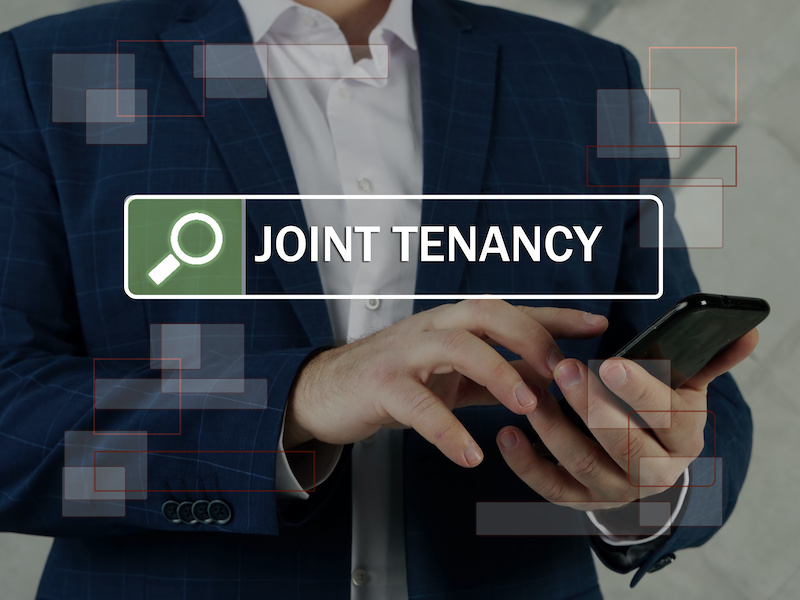 JOINT TENANCY inscription on the screen. Close up Modern Banker hands holding black smart phone. Joint tenancy is a form of property ownership normally associated with real estate. 