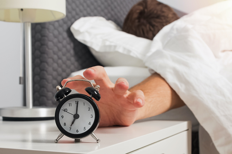 Man's hand reaching out alarm clock on the nightstand early in the morning. Morning routine concept