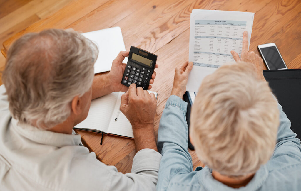 Budget, finance and senior couple with calculator planning financial investments, mortgage and tax papers. Elderly woman counting bills, debt and pension fund on bank statement with partner at home.