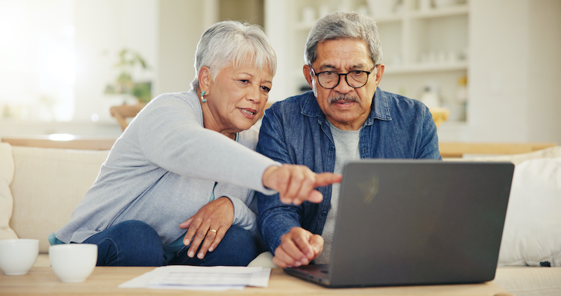 Senior, couple and planning on laptop in living room with document for finances, investment or retirement. Elderly man, woman and pointing by technology for online banking, account balance or savings.