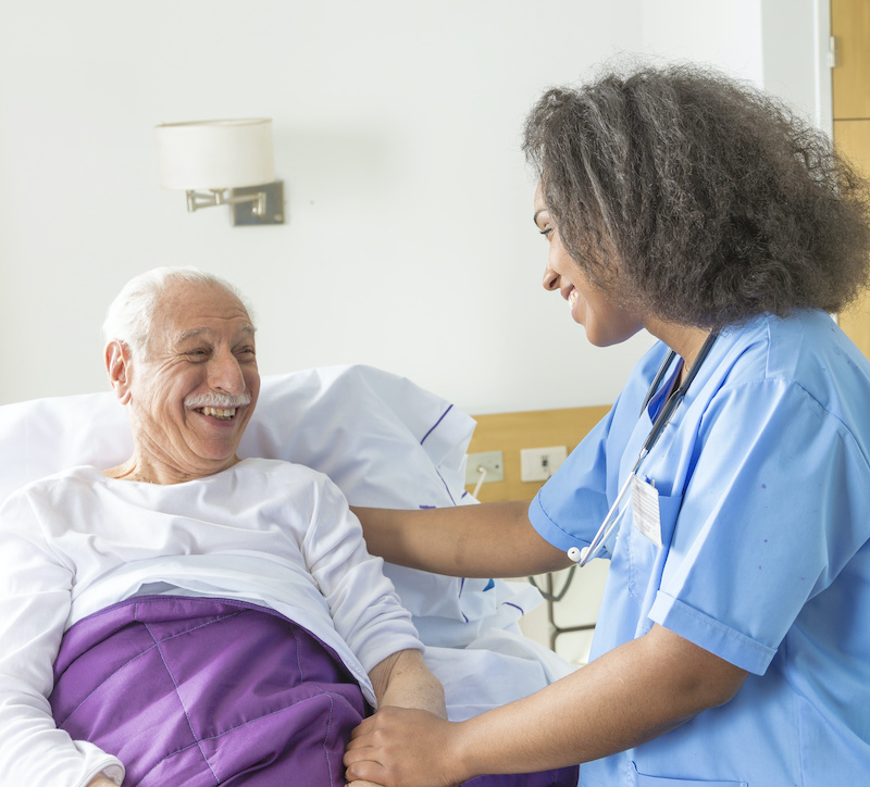 Reassuring confident african female doctor visiting elderly caucasian patient in hospital bed.