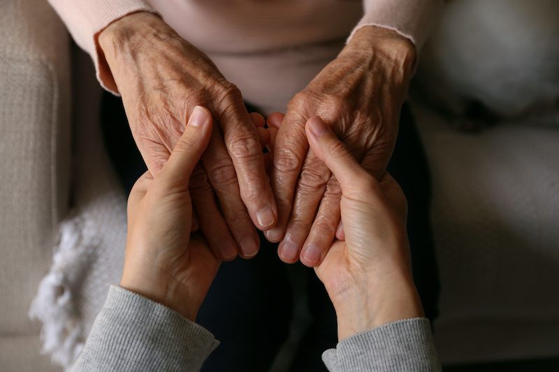 Cropped shot of elderly woman and female geriatric social worker holding hands. Women of different age comforting each other. Close up, background, copy space.