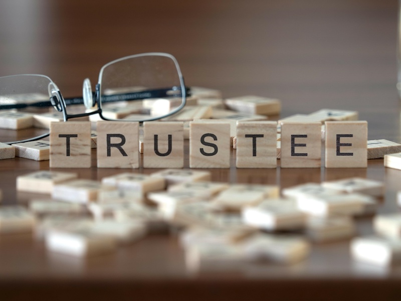 trustee word or concept represented by wooden letter tiles on a wooden table with glasses and a book