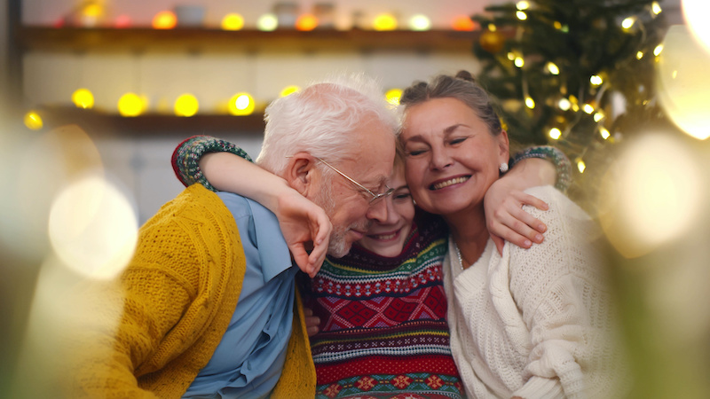 Smiling grandparents and grandson sitting on couch at home. Portrait of loving grandfather and grandmother embracing smiling preteen boy celebrating christmas together