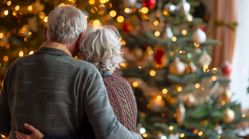 Elderly couple embracing in front of a decorated Christmas tree. Concept of senior love, holiday season, festive celebration, family togetherness.