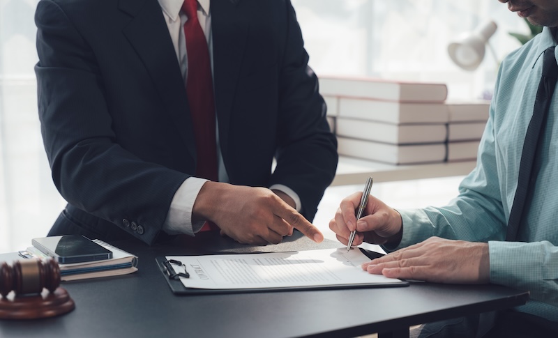 Legal Contract Signing: A close-up shot of a man signing a legal document in a professional setting. An attorney or advisor points to the signature line with a confident air.