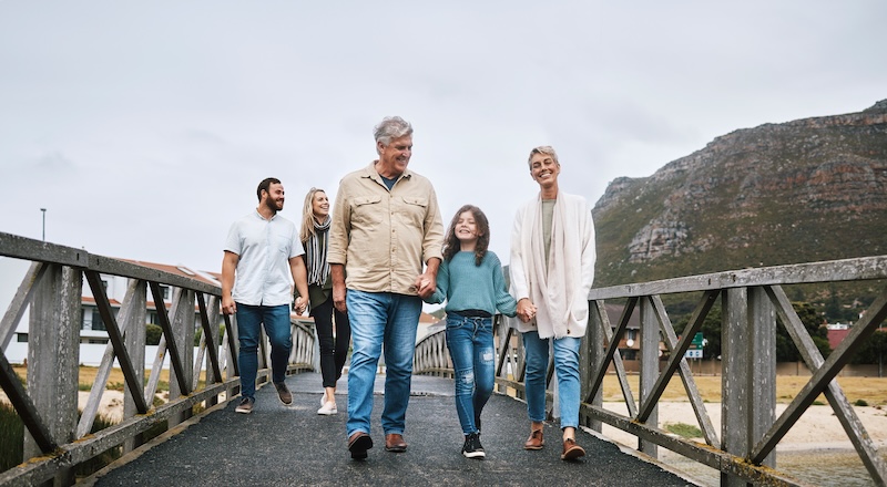 Family, walking and travel with a girl and grandparents holding hands on a pier while on holiday or vacation together. Love, trust and children with a man, woman and granddaughter boding on a walk.
