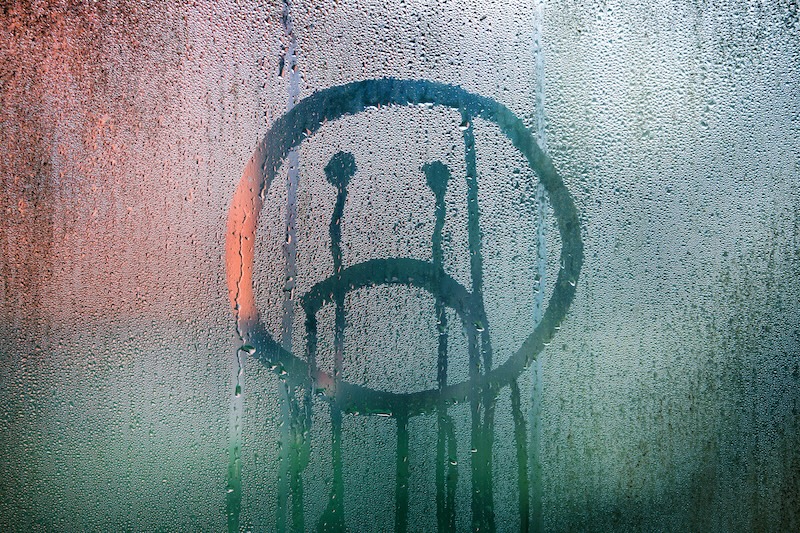 Sad upside down smiley hand drawn symbol on wet glass background.