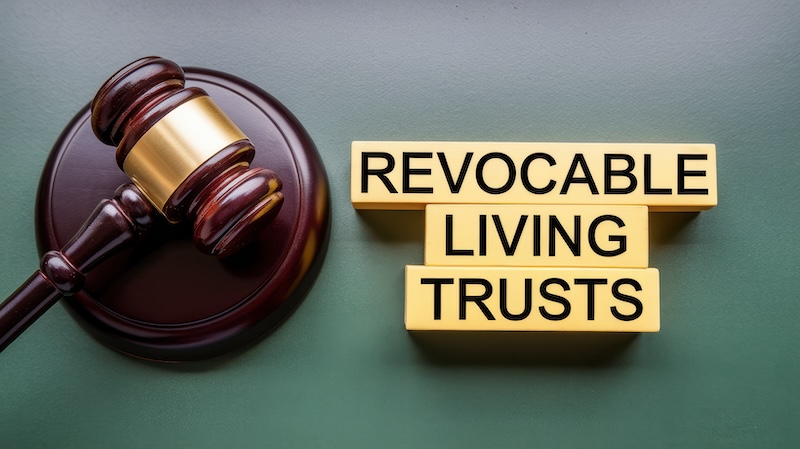 The image displays a gavel alongside wooden blocks spelling out "revocable living trusts" symbolizing legal and financial estate planning.