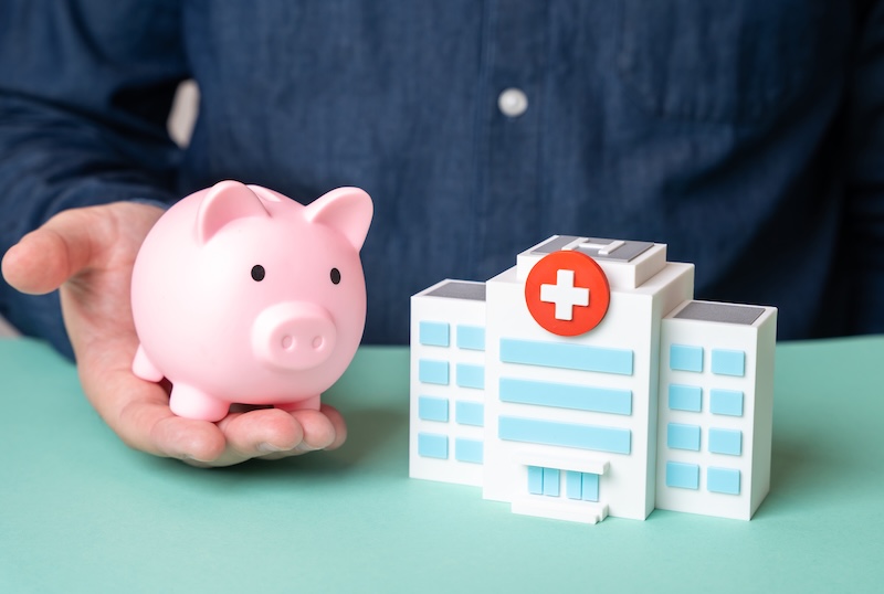 A man holds a piggy bank near a hospital building. Medical insurance. Patient care funding. Affordable coverage. Treatment savings. Insurance policies. Private or public programs. Healthcare access. SSUCv3H4sIAAAAAAAACpyS226DMAyG7yftHVCui0TLYdBXqXZhTFaspkmVhE5T1XdfDlB5t7vDn+3f/mMe729FIUZwhOJYPGIUYlJqcd6CJ6MDrnYrt1JP0nJyt3VXcQDEIzmRN5ZAcTiCx1nDVQaoF6UifqakcB784qSLu6wIwctz0MjwJZEXPuW42BIpGTpCSogdY24ZE9tQFv9XZ/74fBk+S40/aWFmxEolIRs55VJx+fbSXrk1WCYyzNXdIKhYUDMloBtY+NN3s4Skz4wYP6e7bEpoFu1t3OplRihjbjCq+OpfYYzc+AzOhfJp42w2hr/AXNkcbXzytKqKKRwnhvu6qap91Qxt1/cfbd+1a0E+6ExBJ62zCYUYLzRxVxQ3ECCxh/3QlYh1XTbtYSzhgH2JdYOywWbAsQu3eP4CAAD//wMAYEbTPLkCAAA=