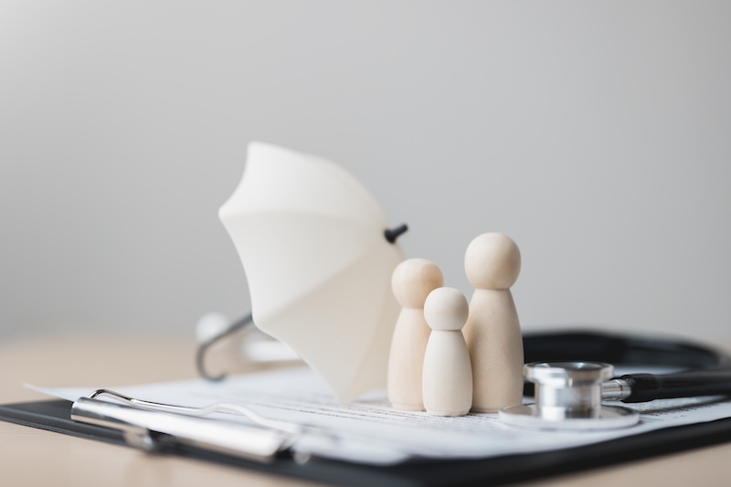 life, insurance, family, protection, beneficiaries, benefit, coverage, term, premium, Wooden family figures with umbrella and stethoscope on insurance documents, symbolizing life and health coverage.