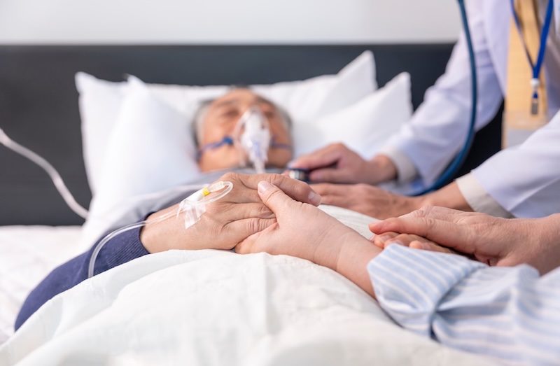 scene of a wife holding hands hopeless senior male patient who have oxygen and intravascular solution drip lying on bed,doctor examining a dying patient,concept of palliative care,end of life care