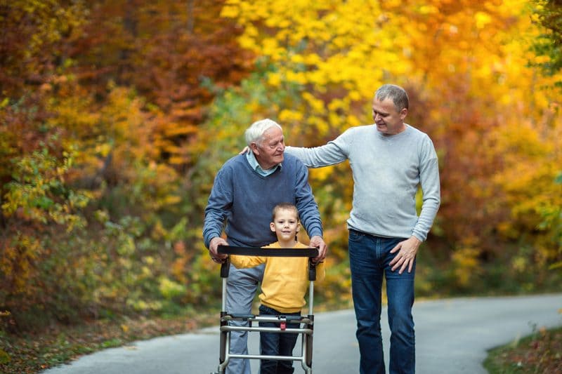 Grandfather with a walker, his son and his grandson walking together in autumn