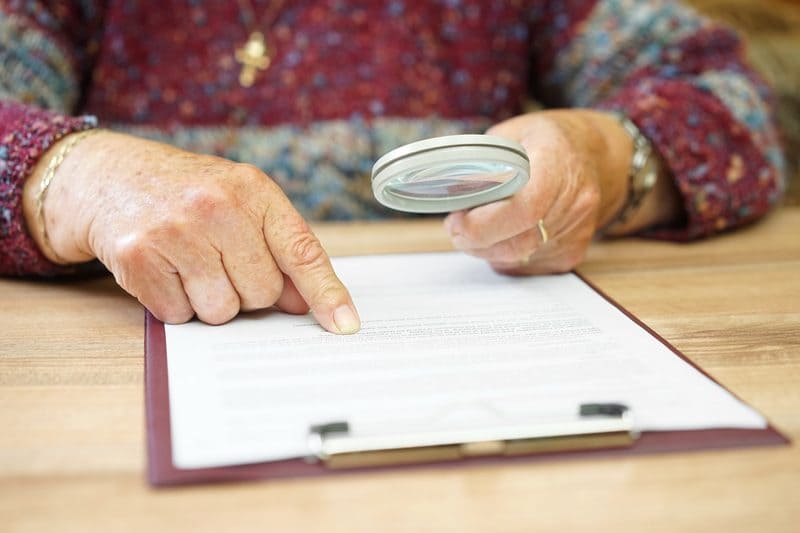 Older person reading a document with a magnifying glass
