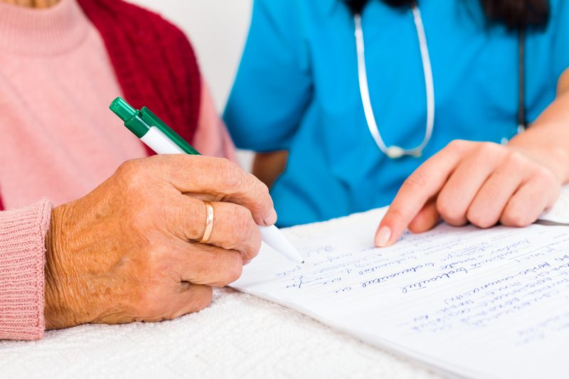 Older woman signing a form with a nurse beside her